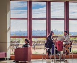 Three students sitting by large window in CELS building overlooking the NY skyline.