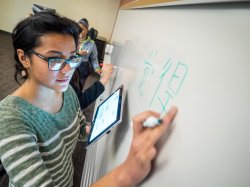 Student writing in Chinese on white board in language course.