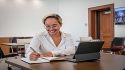 Student smiling while taking notes and using an iPad.