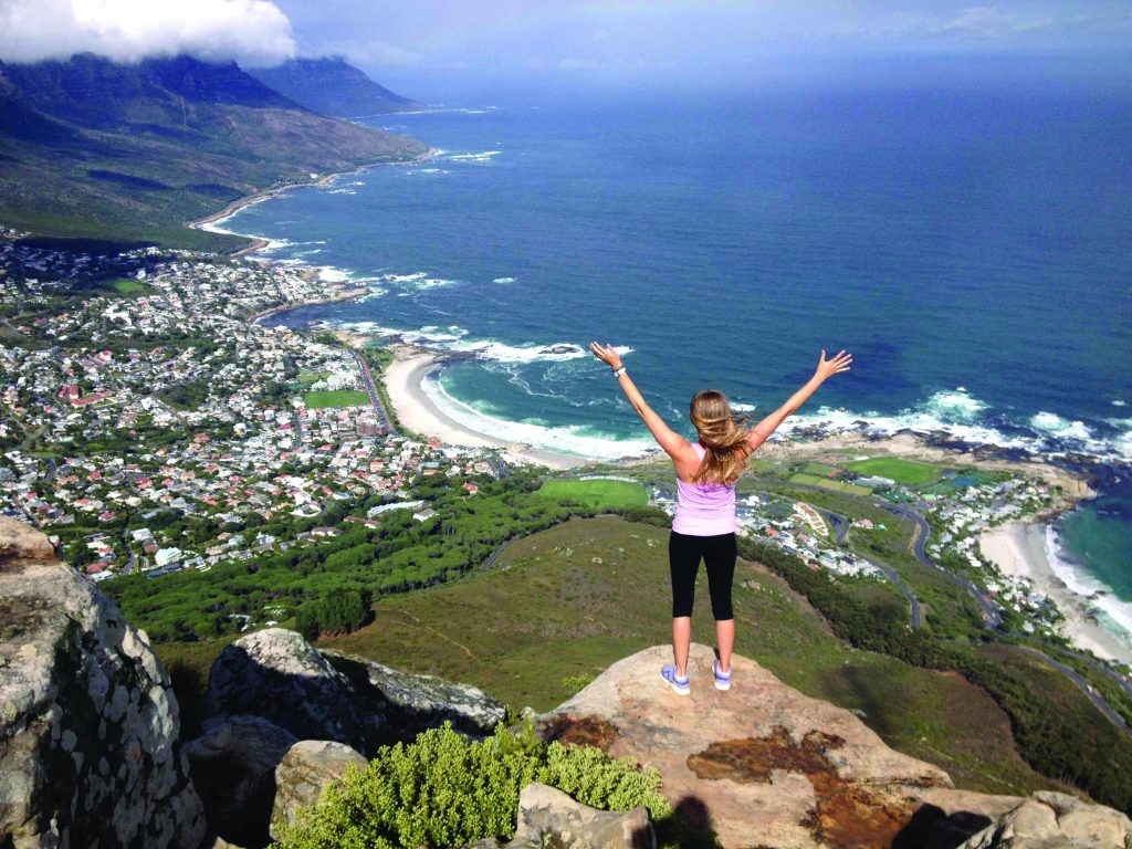 Girl with hands raised standing on a cliff overlooking the ocean